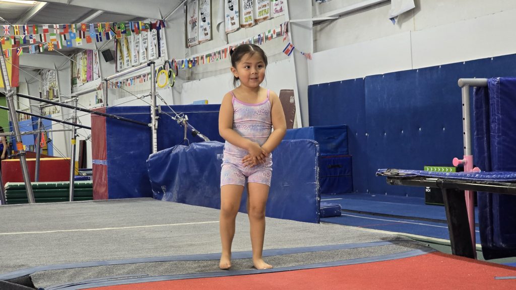 Little girl in gymnatsics attire waiting at the beginning of the mat.