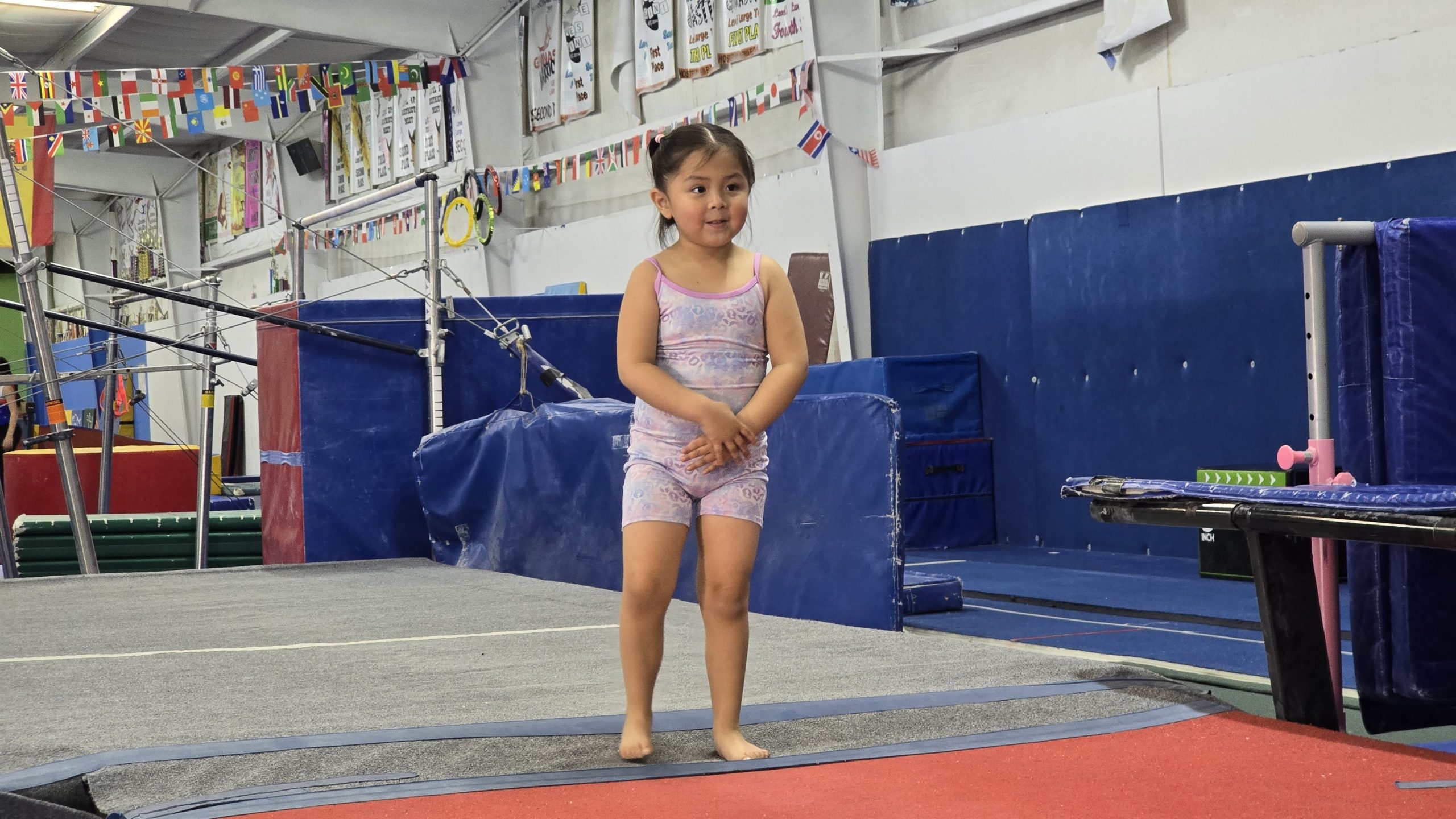 Little girl in gymnatsics attire waiting at the beginning of the mat.